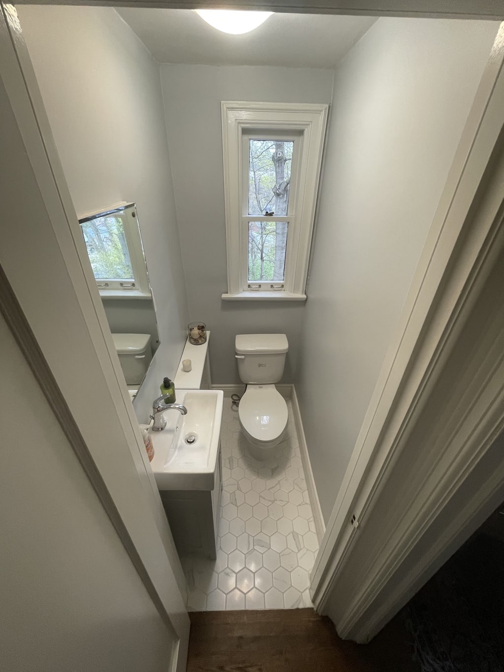 Compact renovated bathroom with a pedestal sink, hexagonal floor tile, and tall window
